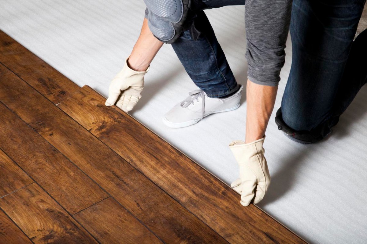 A worker in white gloves installs wood flooring.