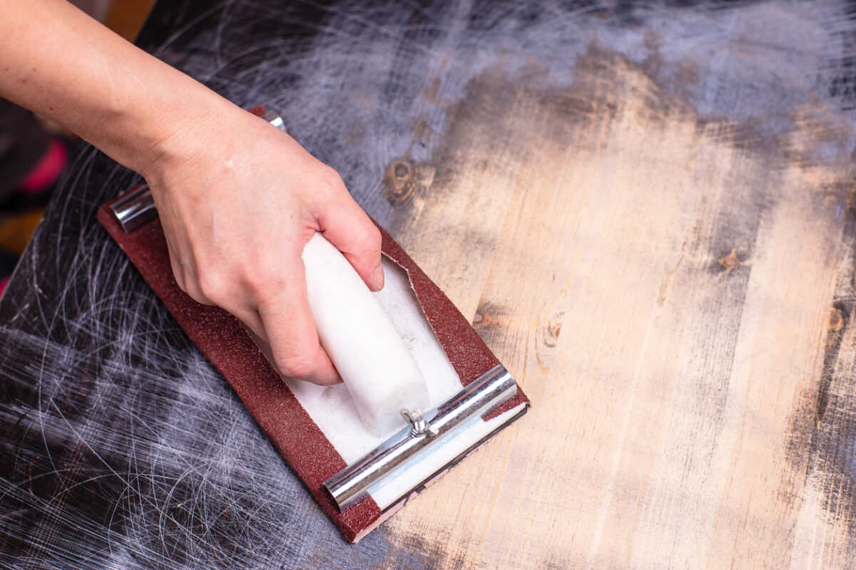 Person sanding finish off of damaged wood furniture.