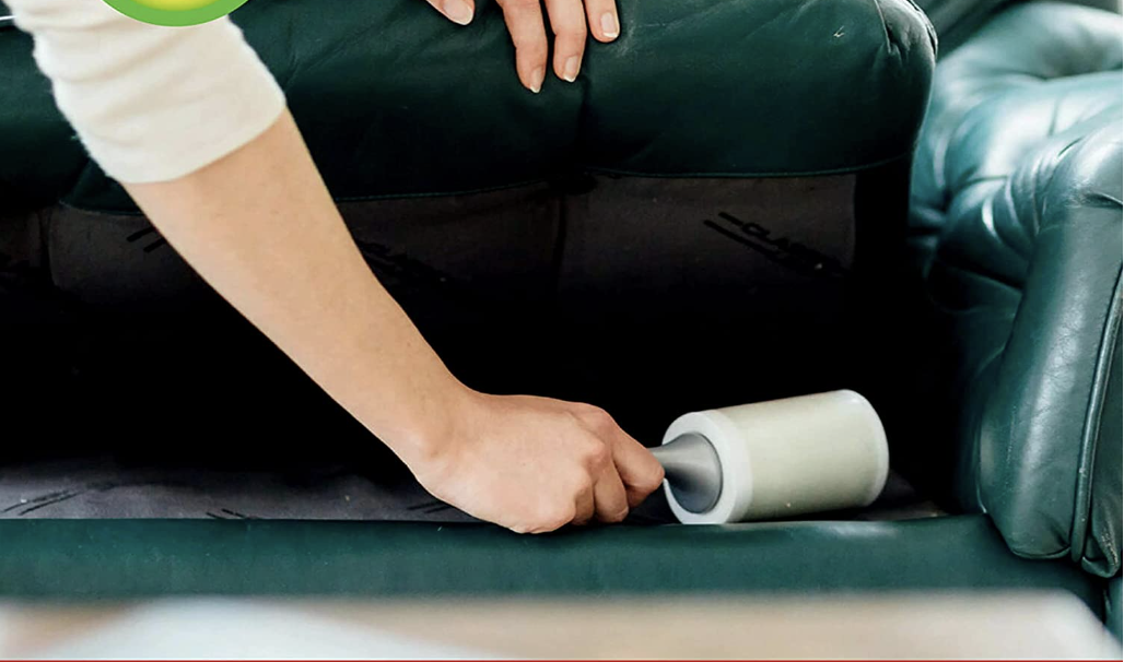 Person uses a lint roller to clean the seat of a couch.