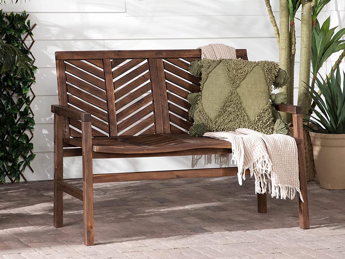 A wooden bench outside on a patio with a cushion and a blanket