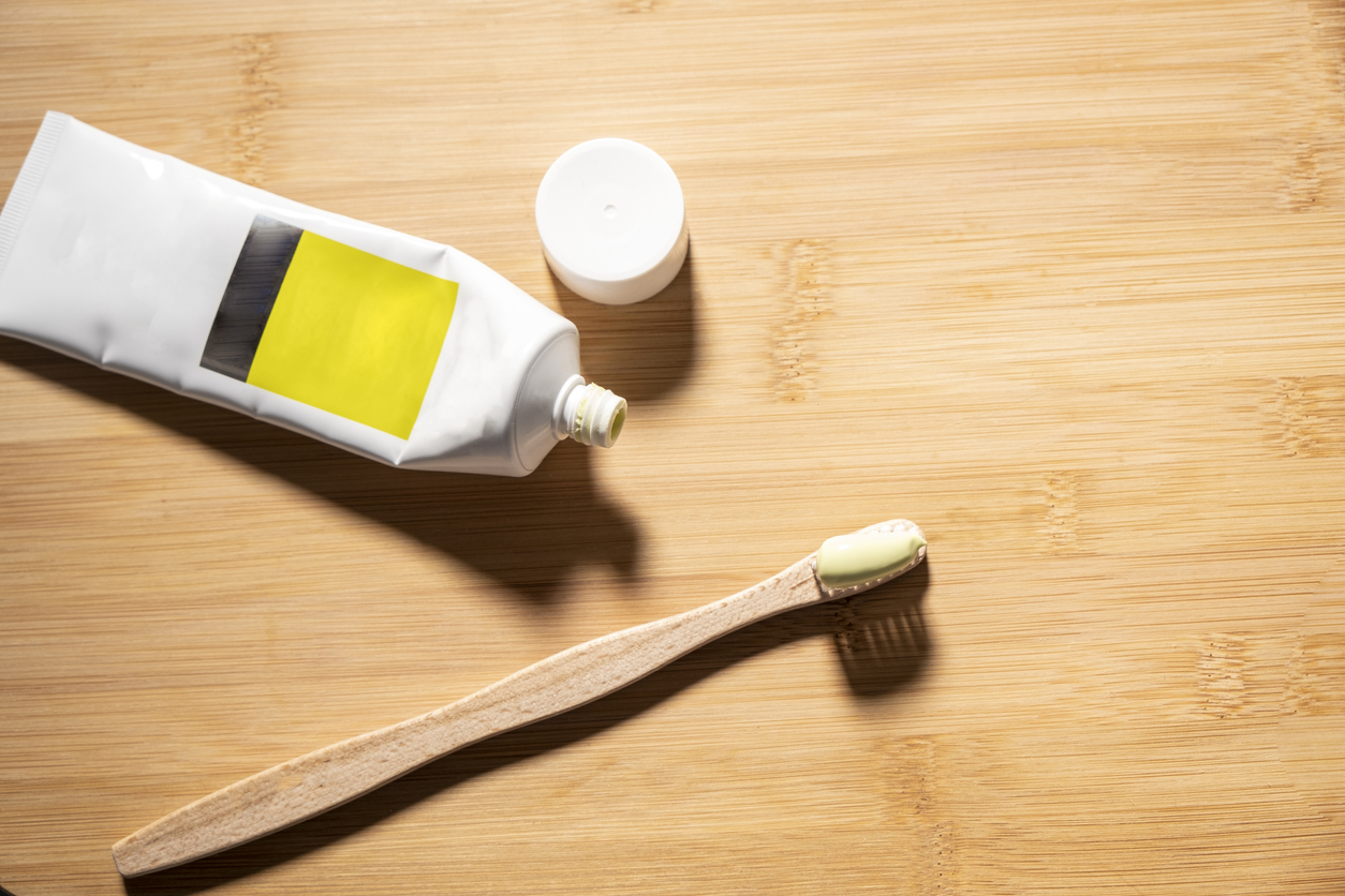 A toothbrush and an open tube of toothpaste on top of a wood table.