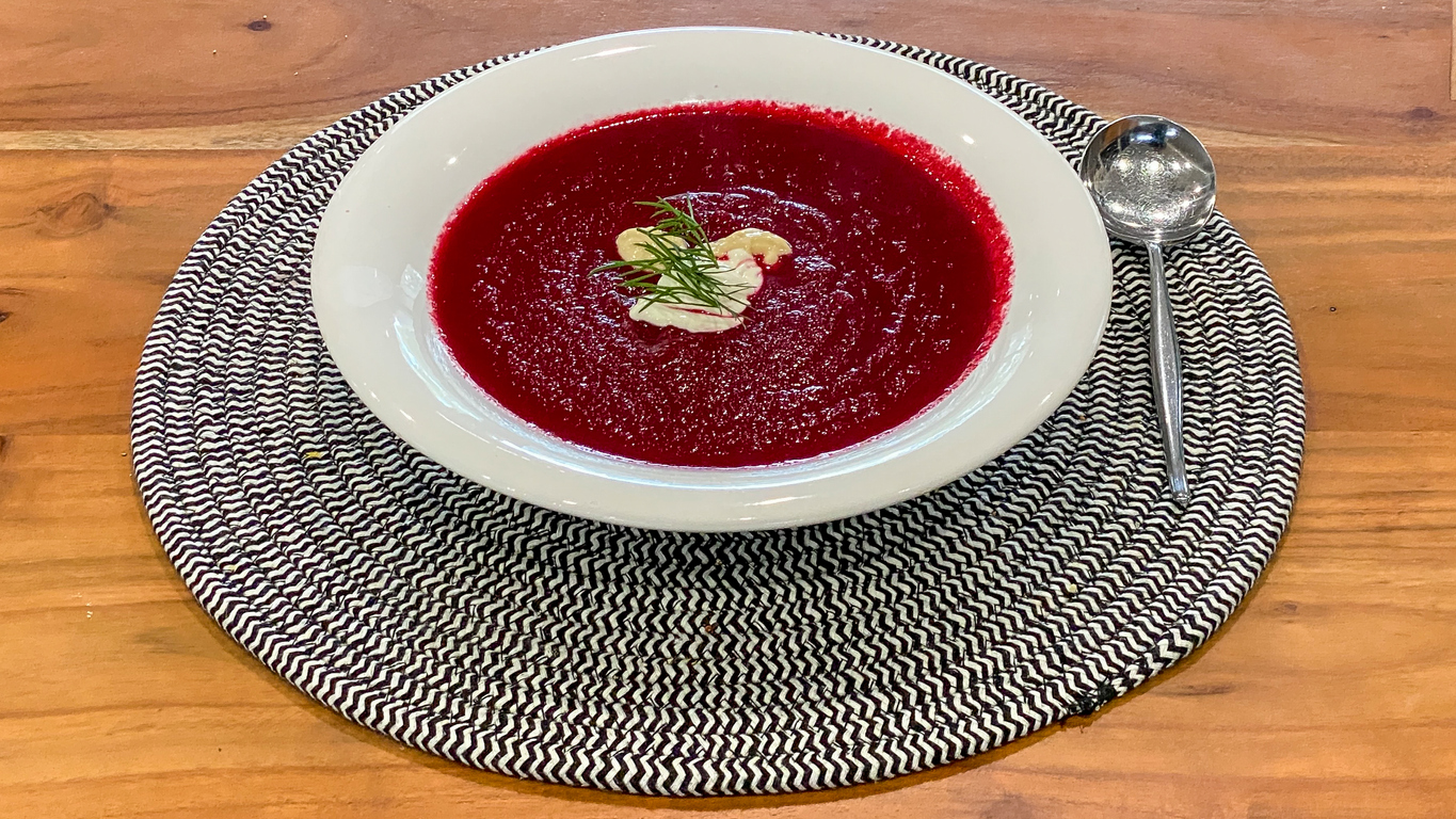 Bowl of borscht on top of a black and white placemat, which is on a wood table.