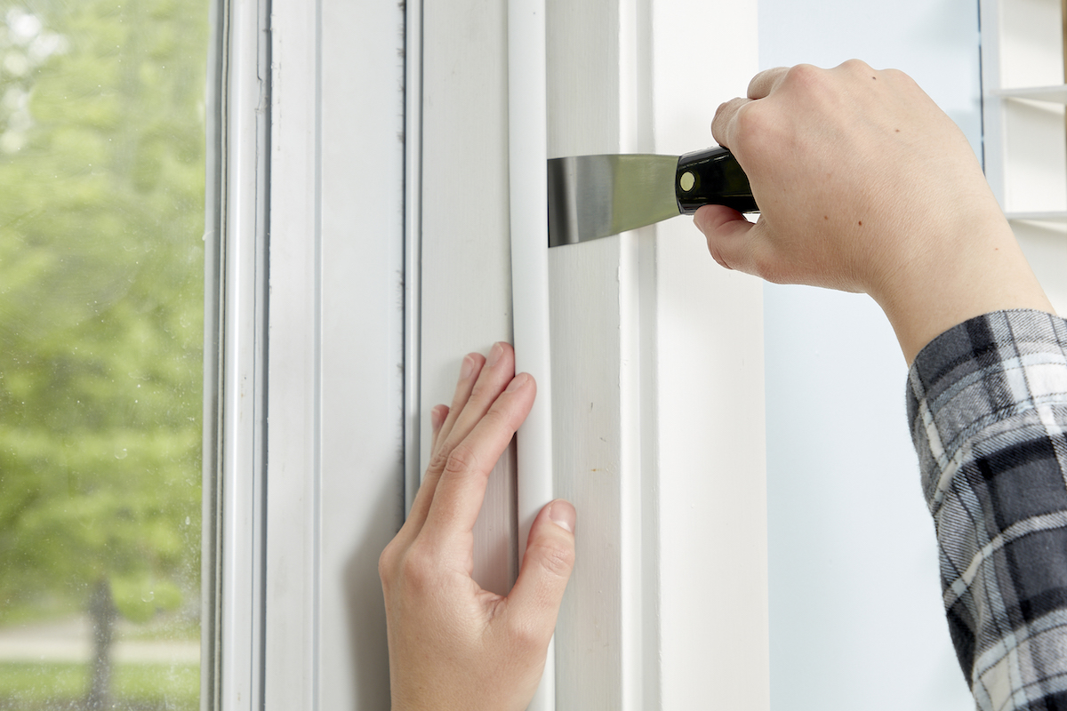 Woman uses a putty knife to apply weather stripping to a front door. 