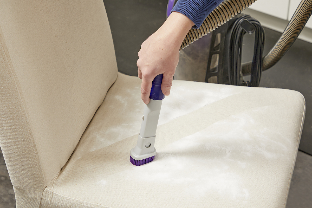 Woman uses vacuum attachment to vacuum baking soda off the seat of a chair.