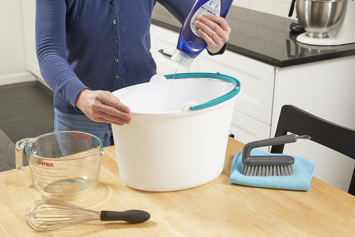 Woman mixing dish soap into a bucket of water to make upholstery cleaner.