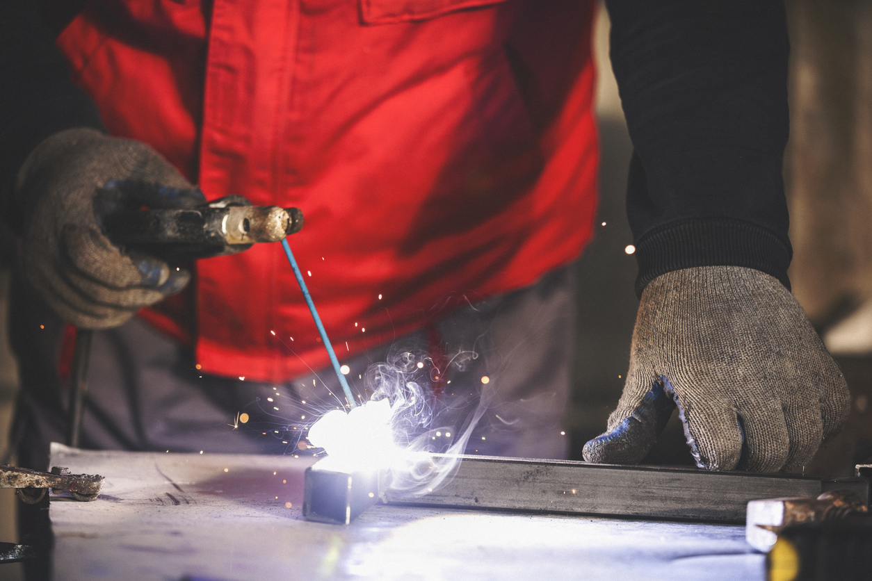 Welder wearing gloves MIG welding a steel bar