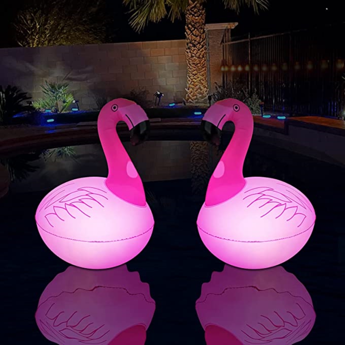 A swimming pool at night is lit by flamingo-themed party lights.