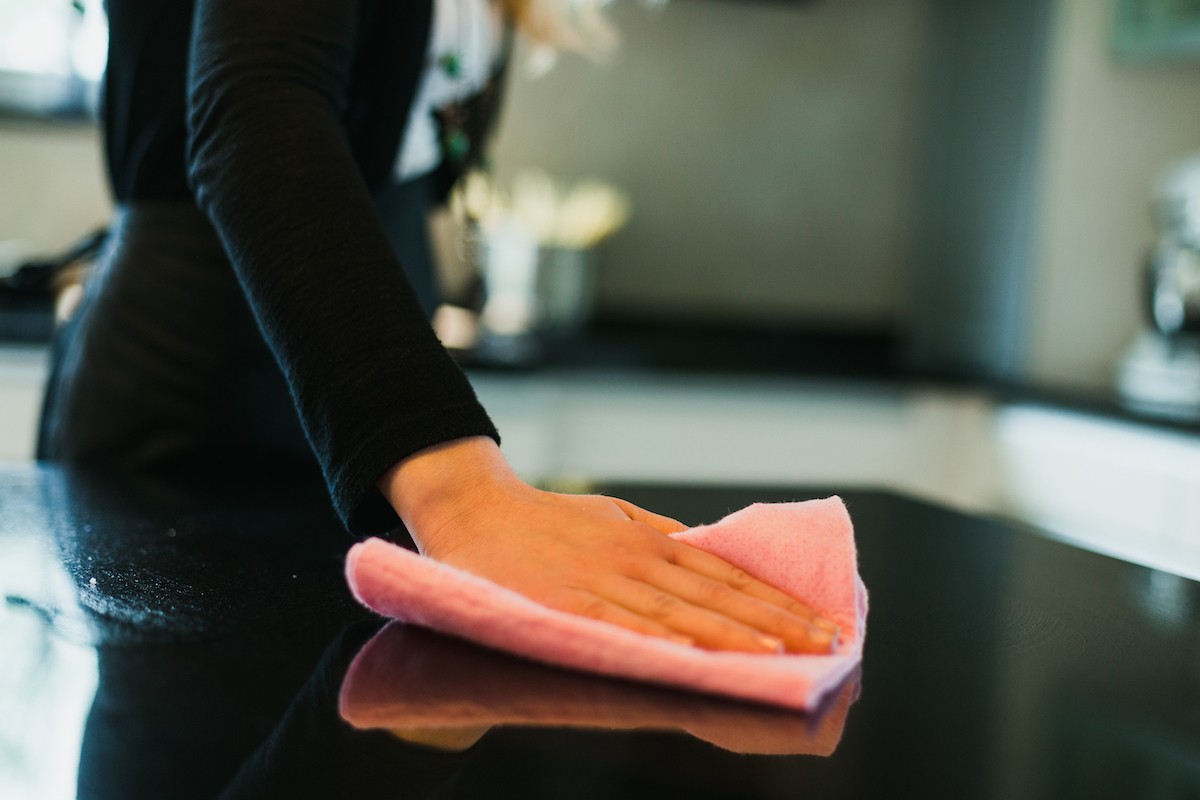 Close-up of a woman cleaning a black kitchen countertop with a pink rag.