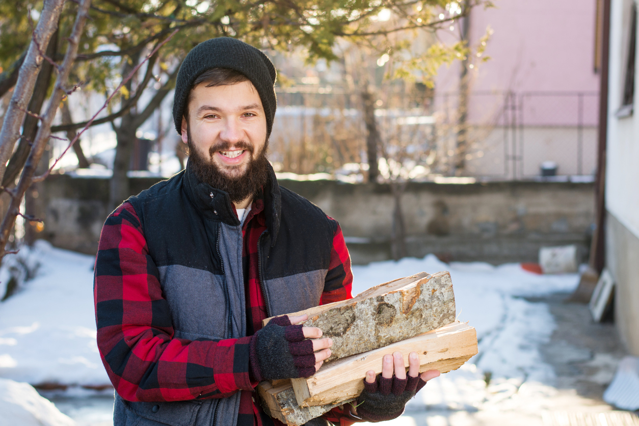 Man in a vest and a buffalo check fleece carrying firewood.