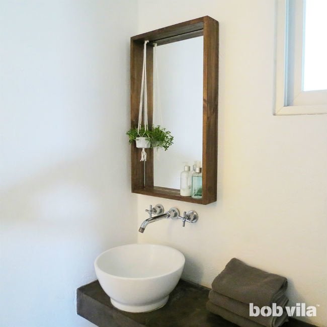 DIY wood-framed bathroom mirror with a small hanging plant over a round vessel sink