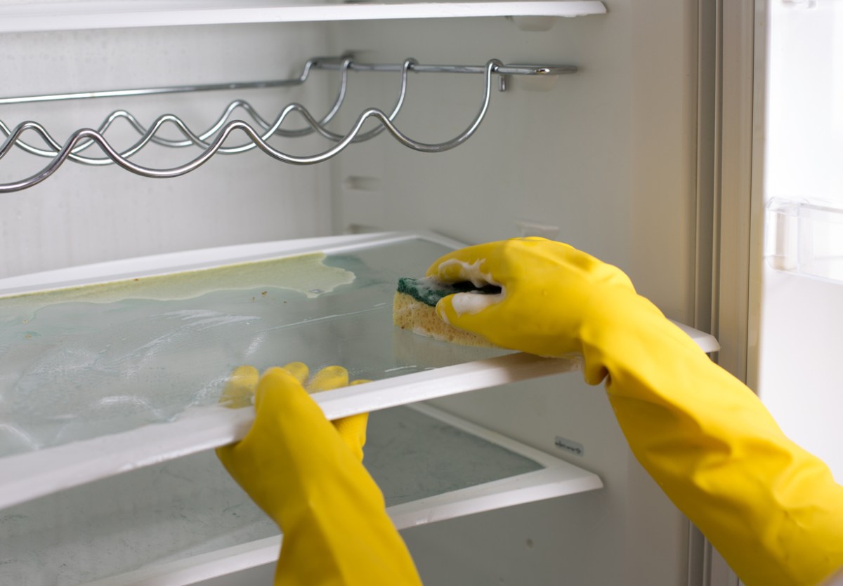 A close up of a person in yellow cleaning gloves deep cleaning an empty fridge.
