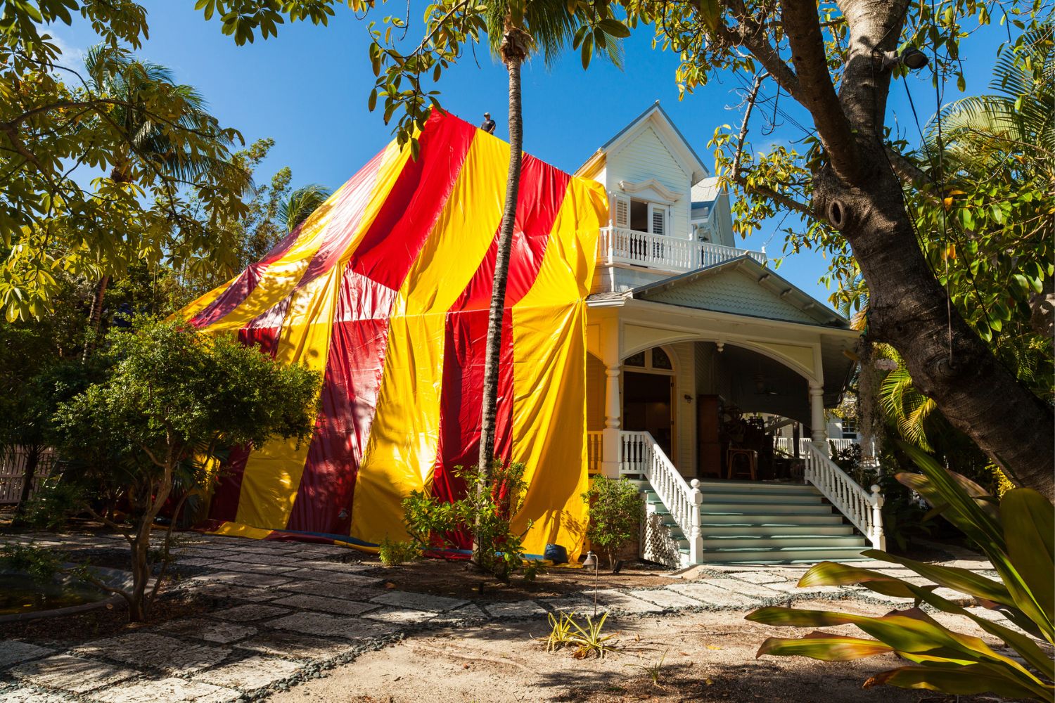 Workers are covering a house with a red-and-yellow tent before fumigation.