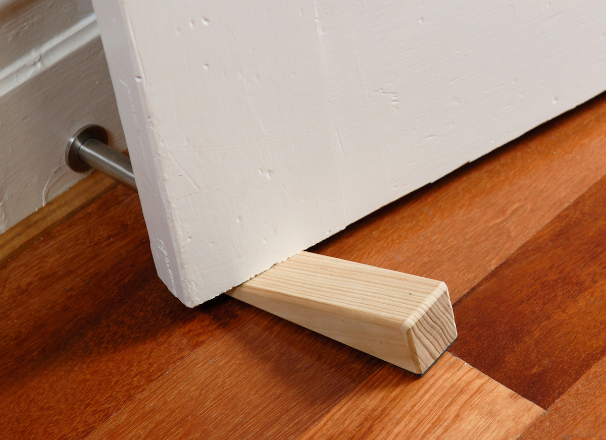 A wooden doorstop made of pine is being used to wedge open a door.