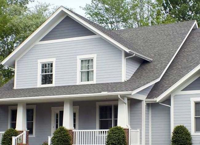 A light gray and blue home with a front porch, white trim, and shrubs. 