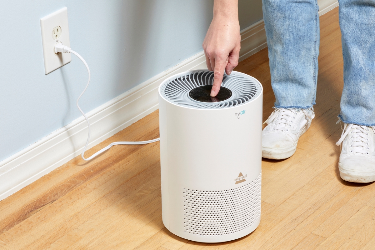 A person is turning on the air purifier machine on the floor.