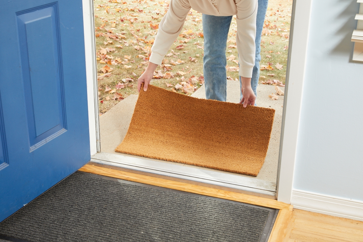 A person is laying a doormat outside of the front door.