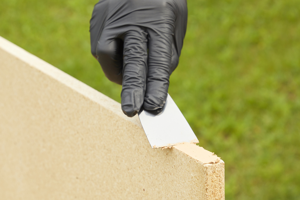 Woman wearing black rubber gloves repairs the edges of particle board with wood filler.