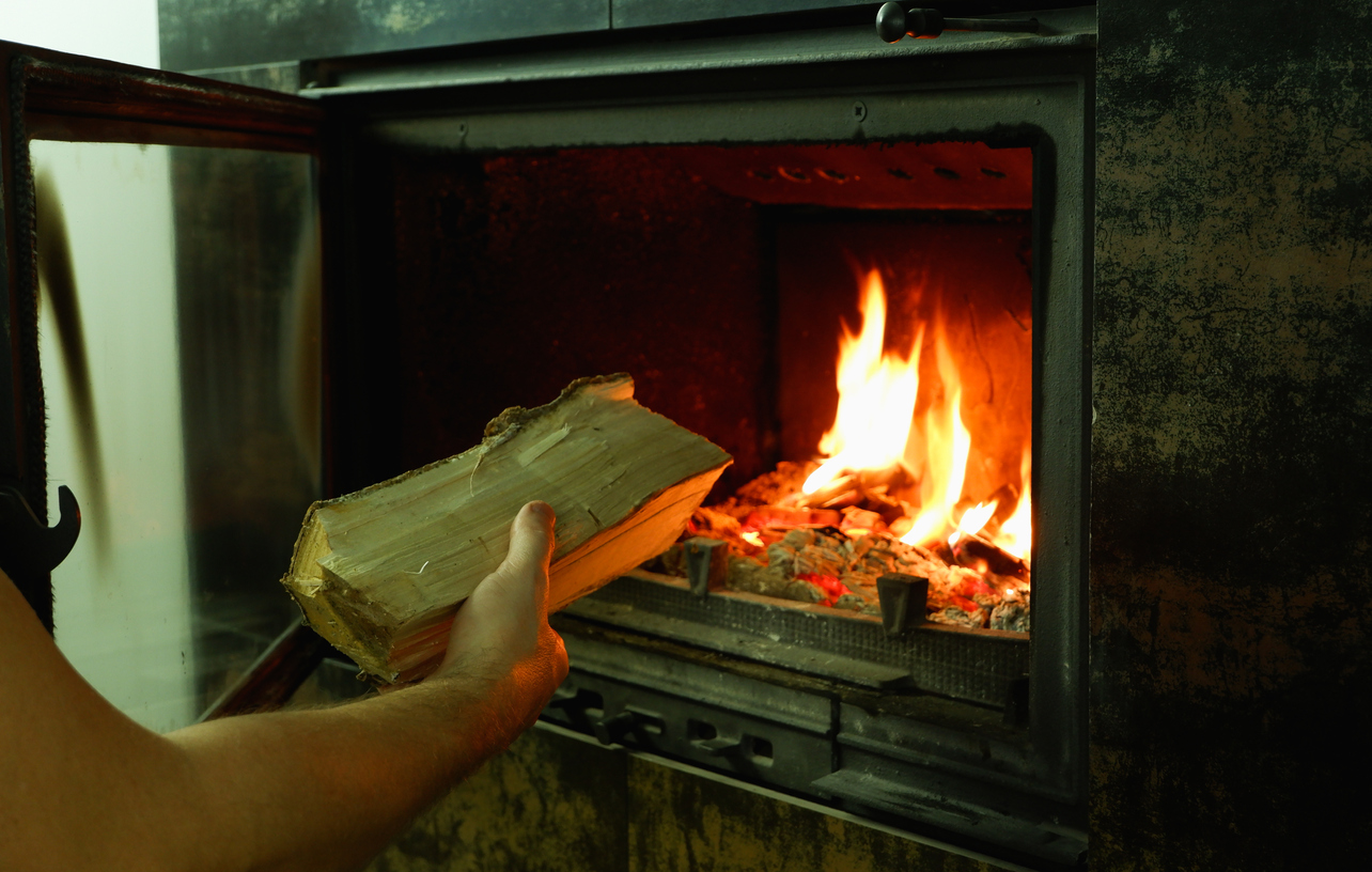 iStock-1394982585 must dos January A man's hand puts wood in the burning fireplace.jpg