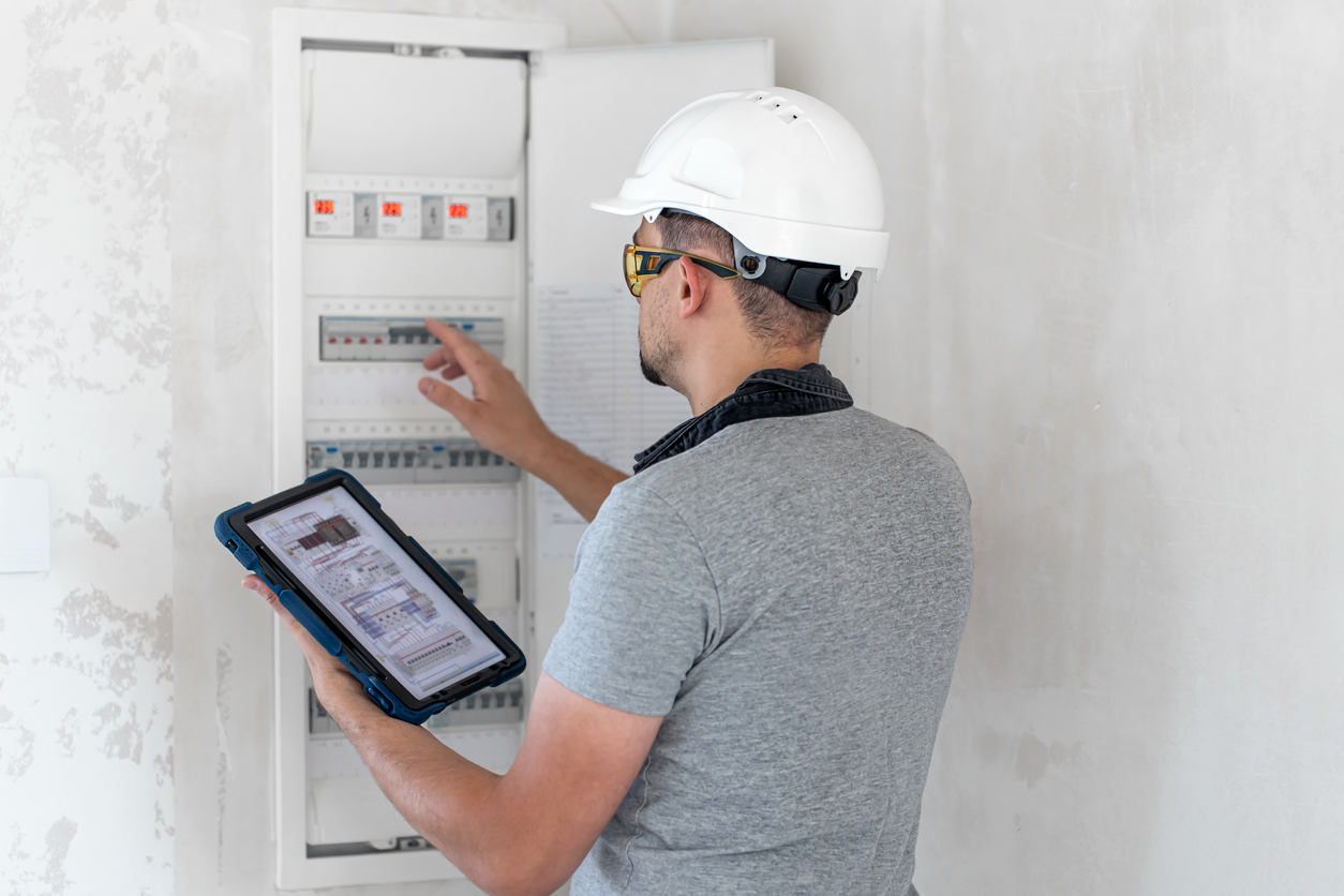 Energy inspector examines home switchboard in hardhat.