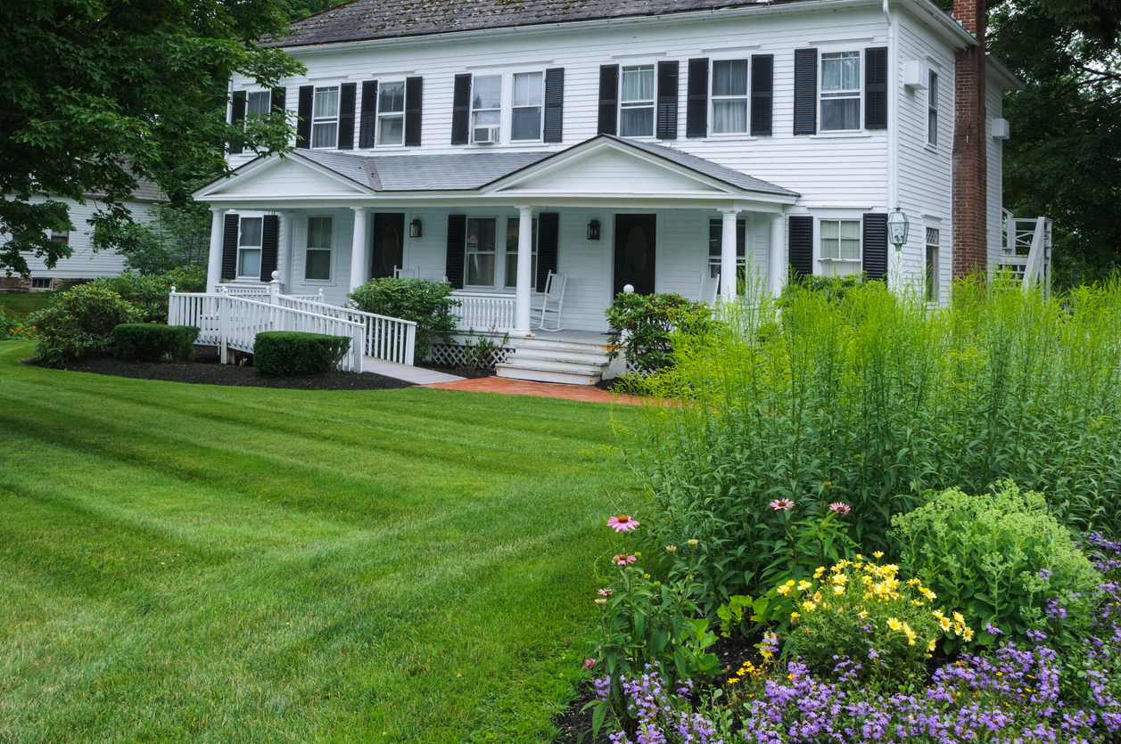 White colonial style home with black shutters and matching wheelchair ramp leading up to front door.