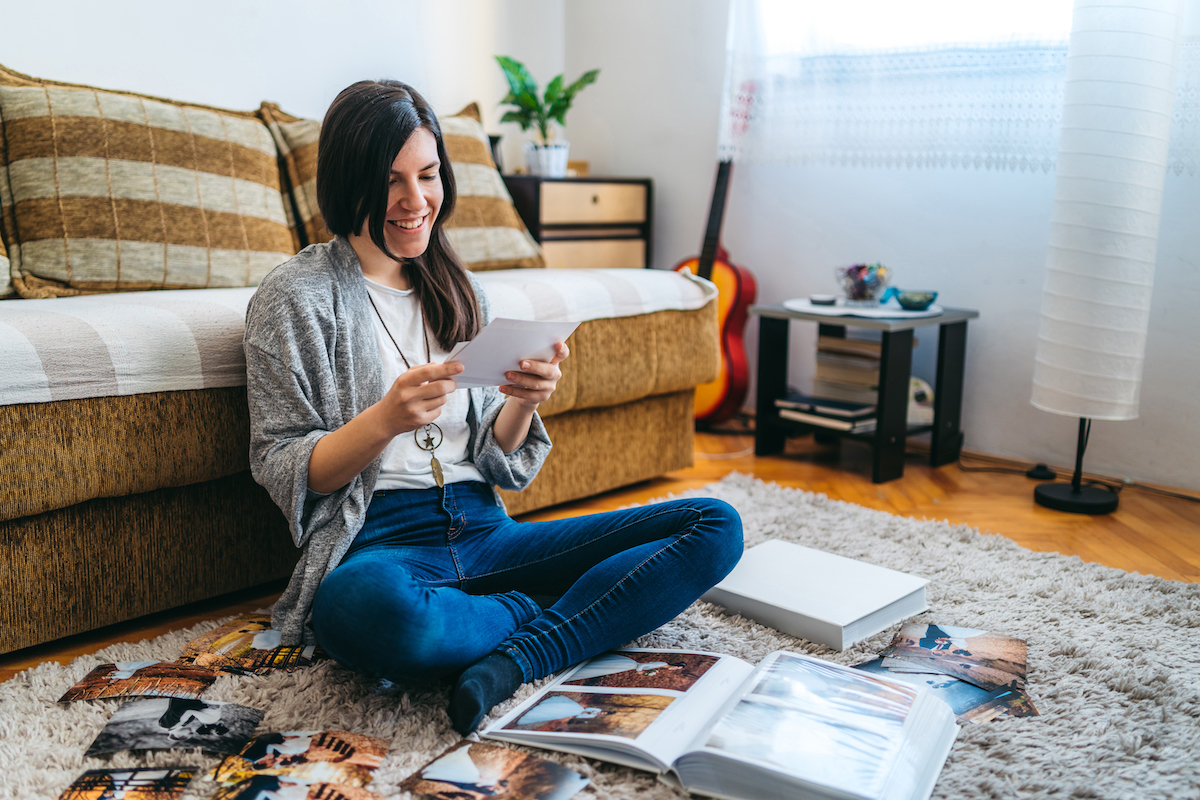 Young woman sitting on her living room floor, looking at photographs and smiling.