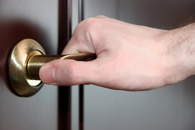 Hand on a lever-style doorknob, on a dark-colored door.