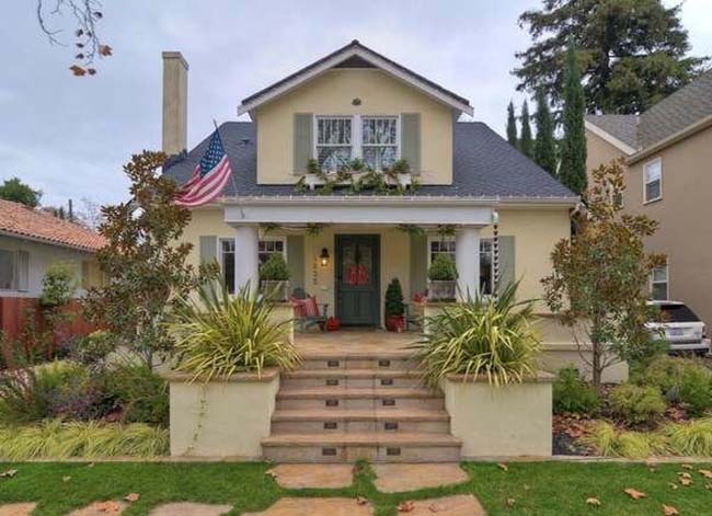 A straw-colored bungalow house with a grey roof and front porch.