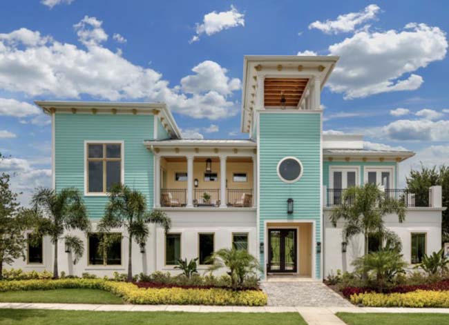 A blocky house in light teal and white with palm trees out front.