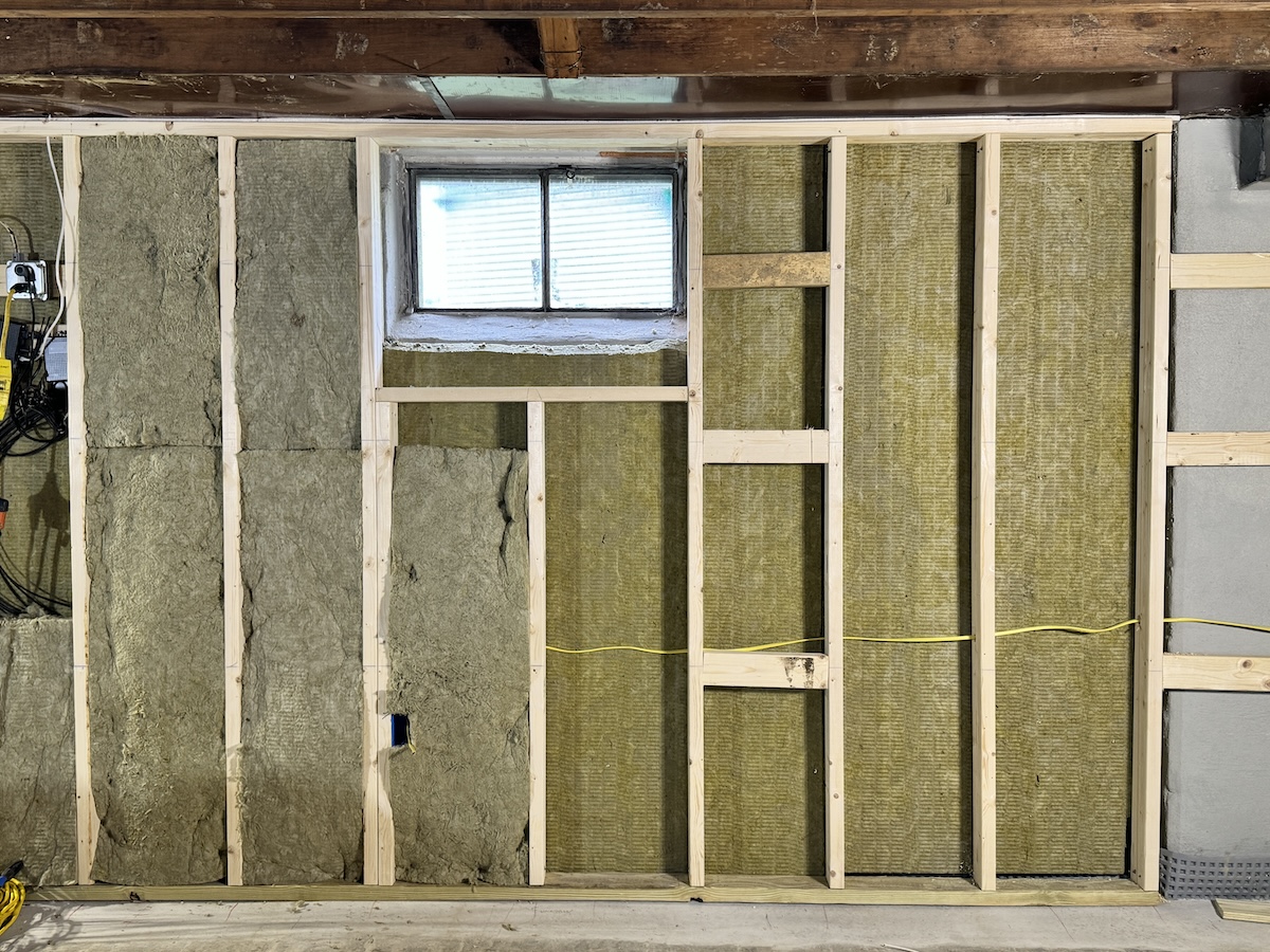 A basement wall stripped for the installation of insulation using 2x4s and rigid insulation boards.