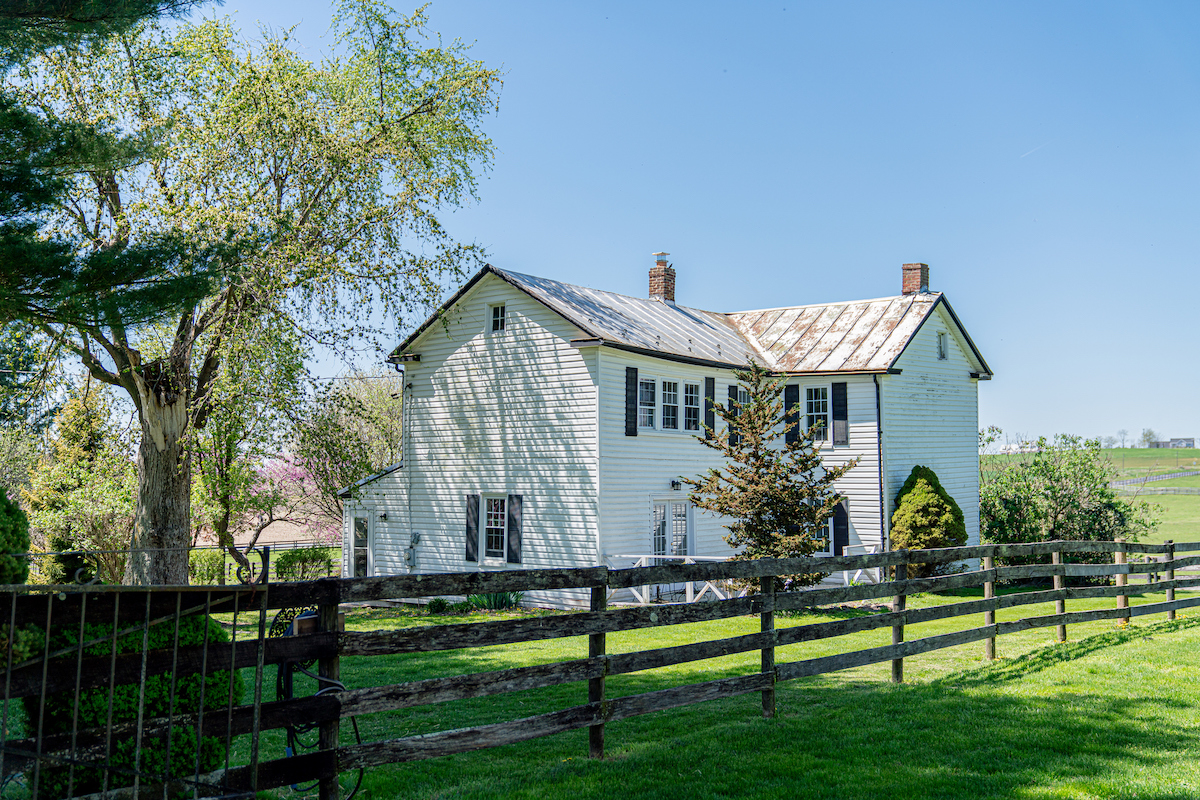 A wooden split rail fence lines the yard of a colonial-style farm home.
