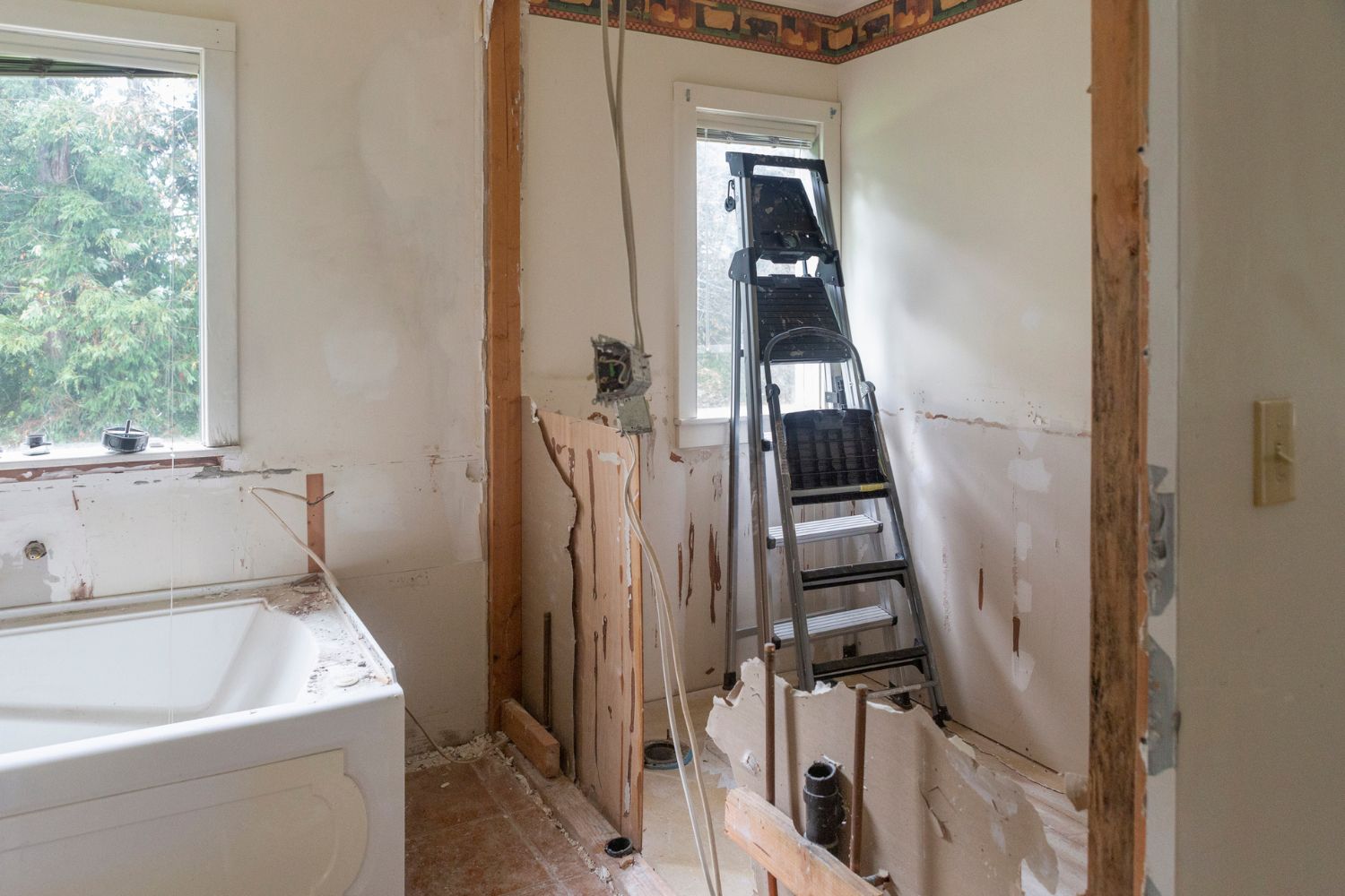 A bathroom has been stripped down for a remodel, with an old bathtub left and a ladder leaning against the window.