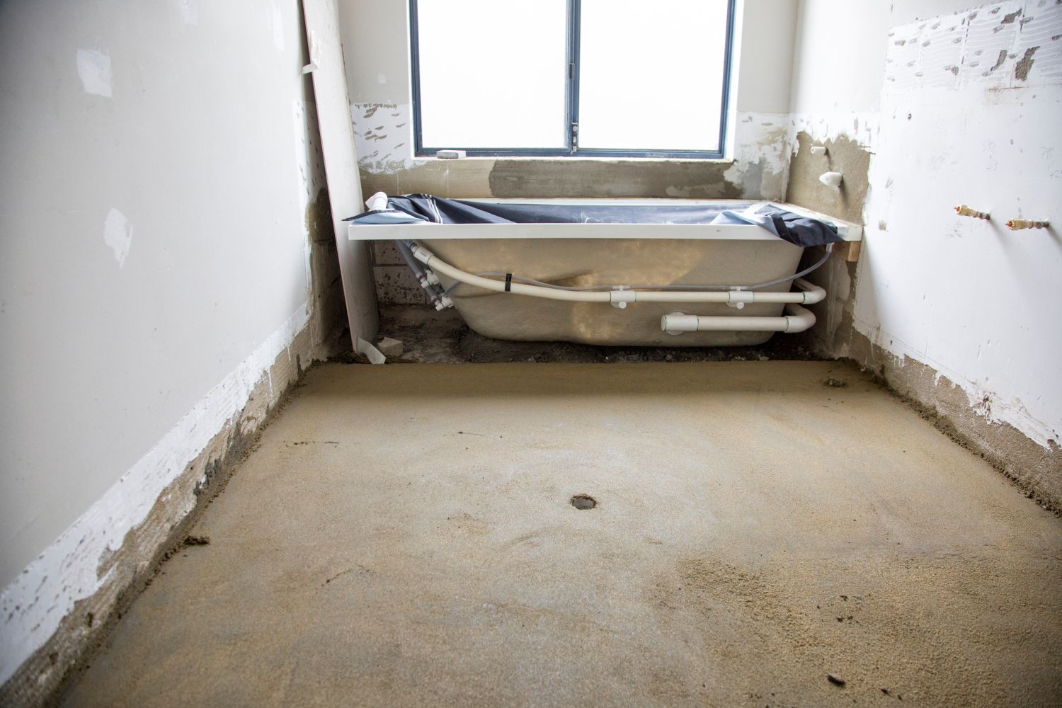 An empty room with plain drywall and no floors and a new bathtub sitting against one wall, waiting to be installed.