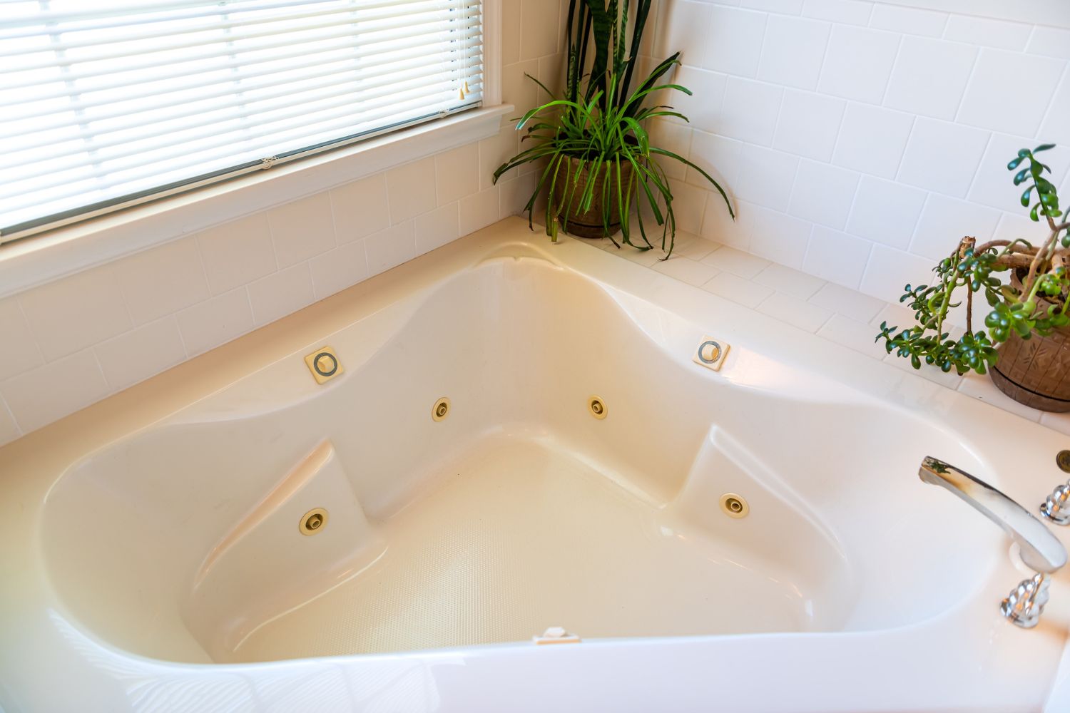 A corner jetted bathtub with two plants on the side shelf.