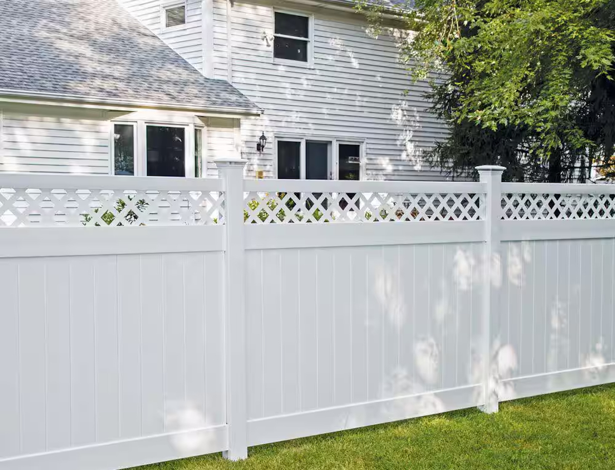 A white lattice top fence is in front of a house with white siding.