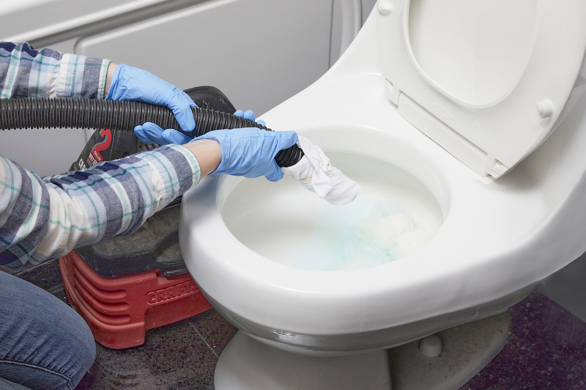 Woman wearing rubber gloves holds the tube of a shopvac over a toilet bowl.