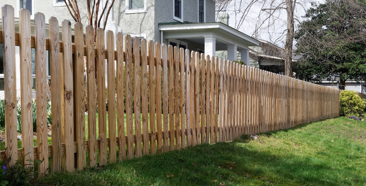 A wooden dog ear fence lines the front yard of a neighborhood home.