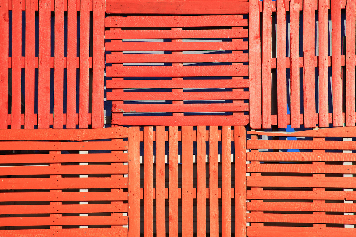 Several repurposed wooden pallets painted orange-red are arranged into a fence.