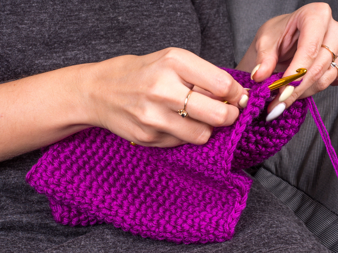 iStock-847404880 how to crochet for beginners woman crocheting a scarf with purple yarn