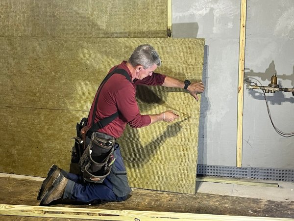 A man in a red shirt prepares wall insulation for a basement.