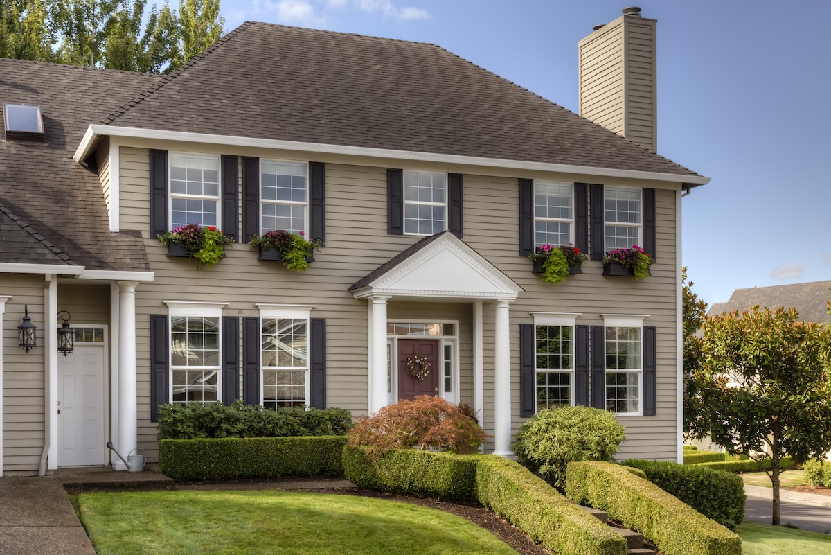 A traditional colonial stle home with taupe siding and black window features.