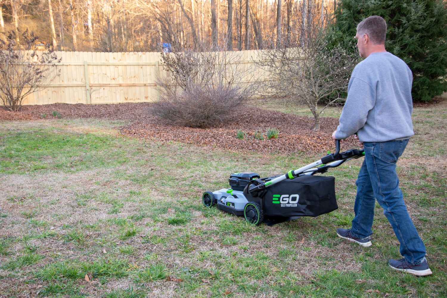 Man in gray sweatshirt cutting grass with an Ego Lawn Mower