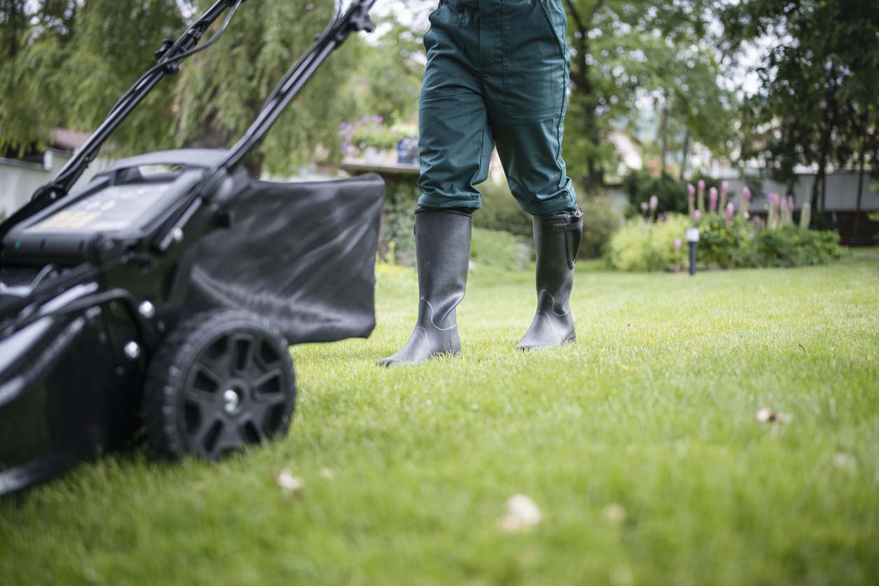 A close up of a worker in boots mowing a lawn.