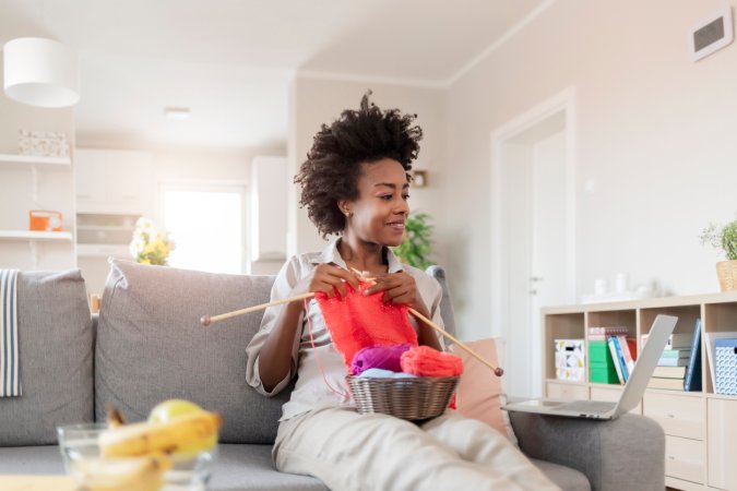 iStock-1287672578 how to knit for beginners iling Woman With Basket With Knitting Yarn and Needles Learn How to Knit Using Website on a Laptop at Modern Home