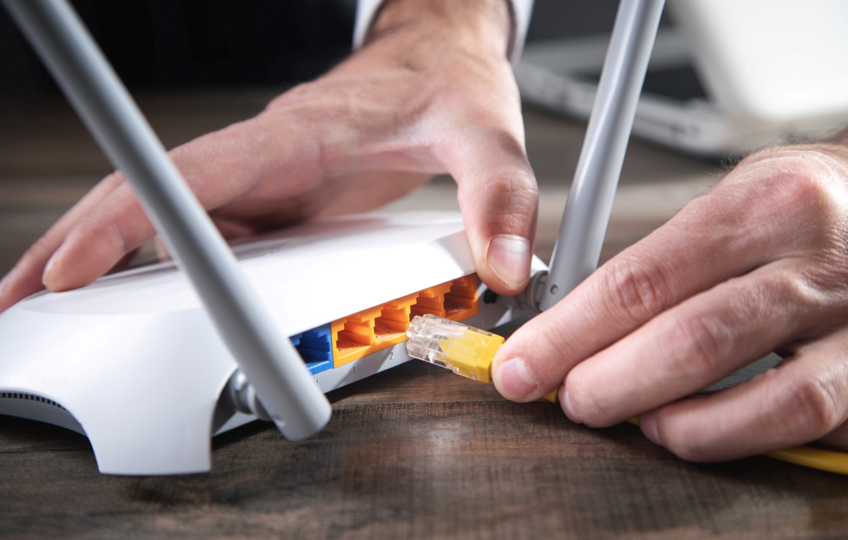 electronics you never clean - hand plugging yellow cord into router