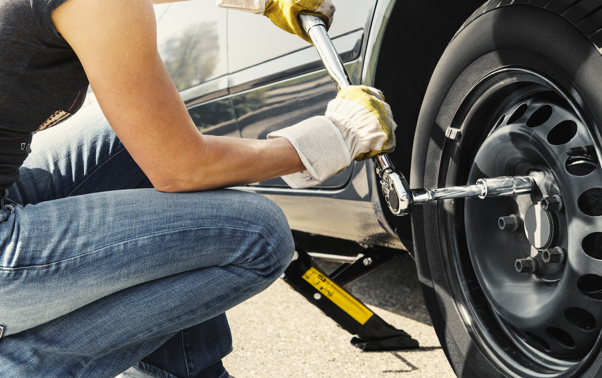 Woman changing tire using torque wrench to tighten lug nuts.