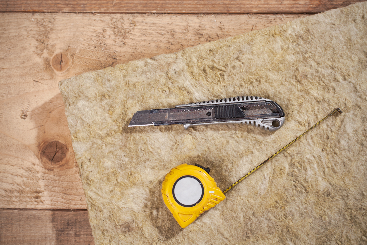 Utility knife and measuring tape sitting atop mineral wool insulation.