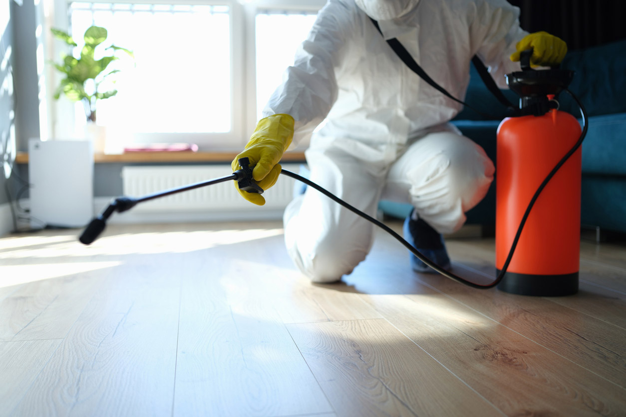 A pest control professional wearing personal protective equipment sprays inside a home to treat a pest infestation.