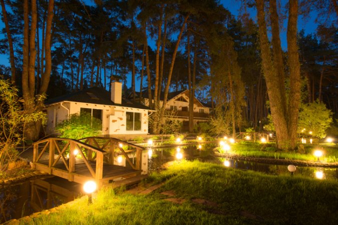 uplighting-landscape-house-with-tall-trees-and-a-pond-with-bridge-at-night