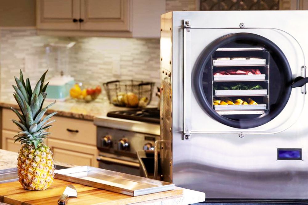 A large freeze dryer sits in a kitchen while filled with several rows of drying fruits and vegetables