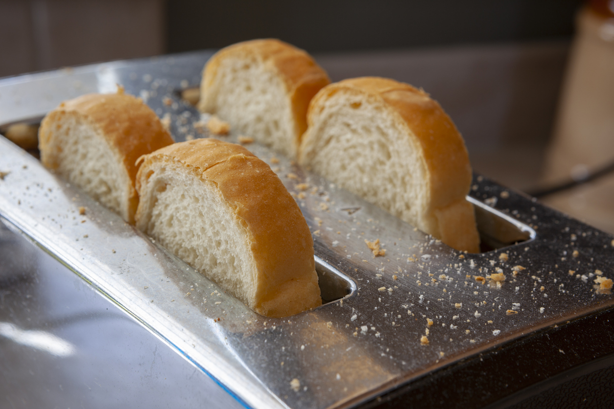 four slices of bread in toaster with crumbs on toaster top